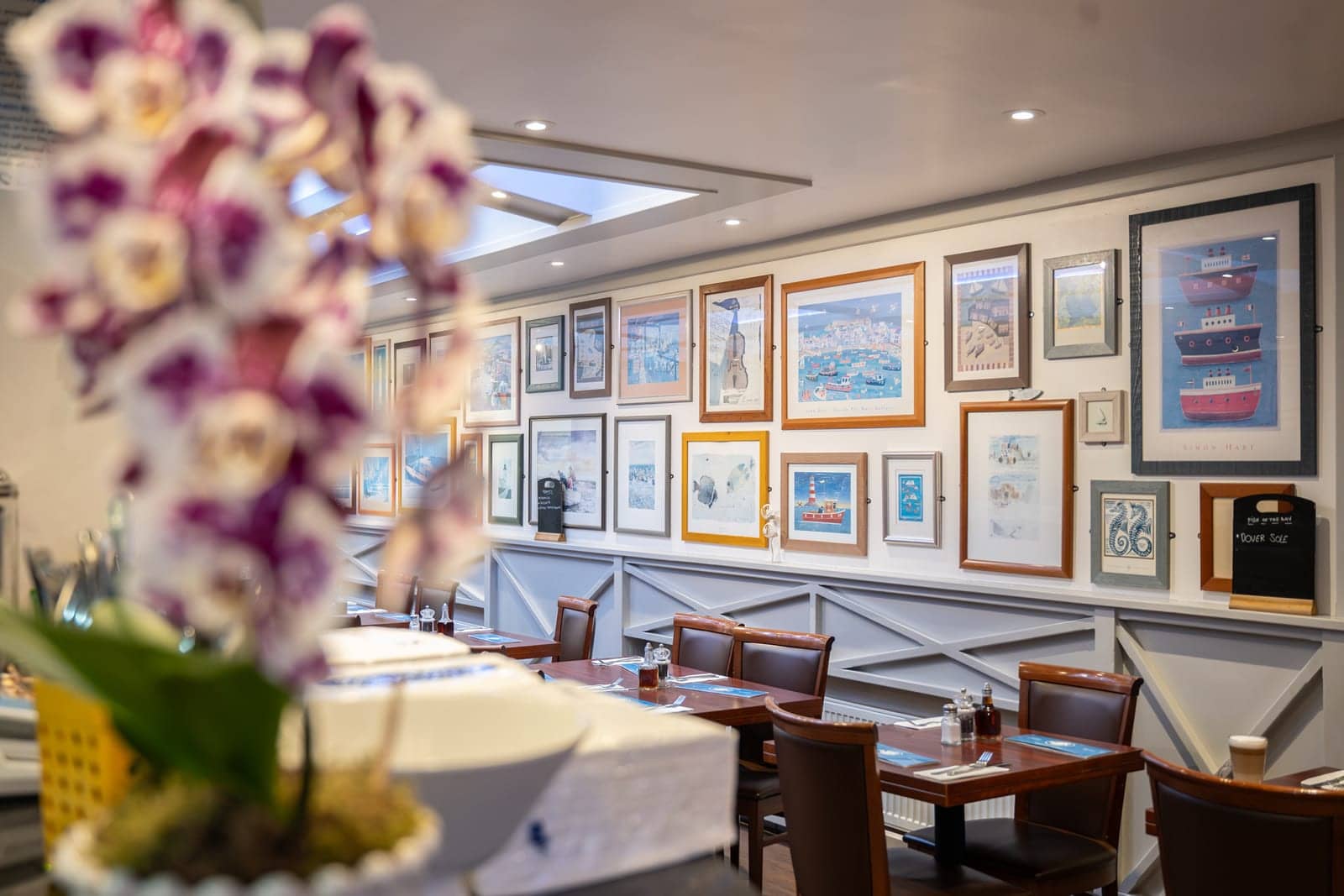 Framed coastal artwork and an orchid in the front dining room