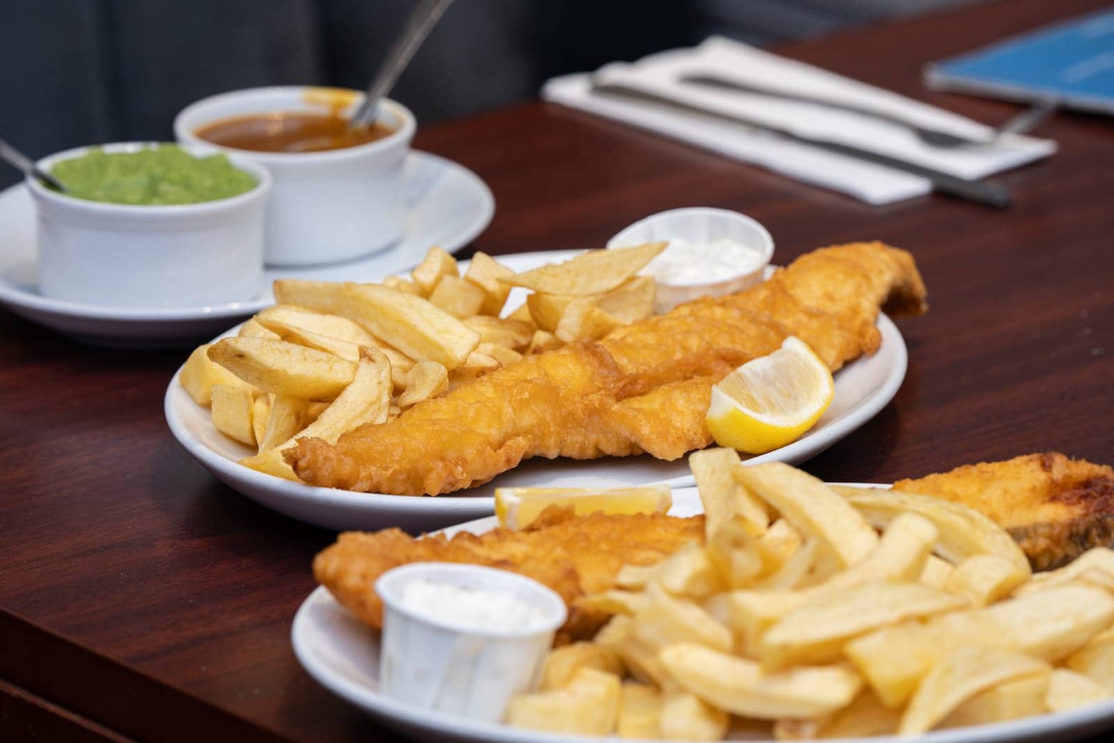 Battered fish and chips with lemon, mushy peas and curry sauce on the side