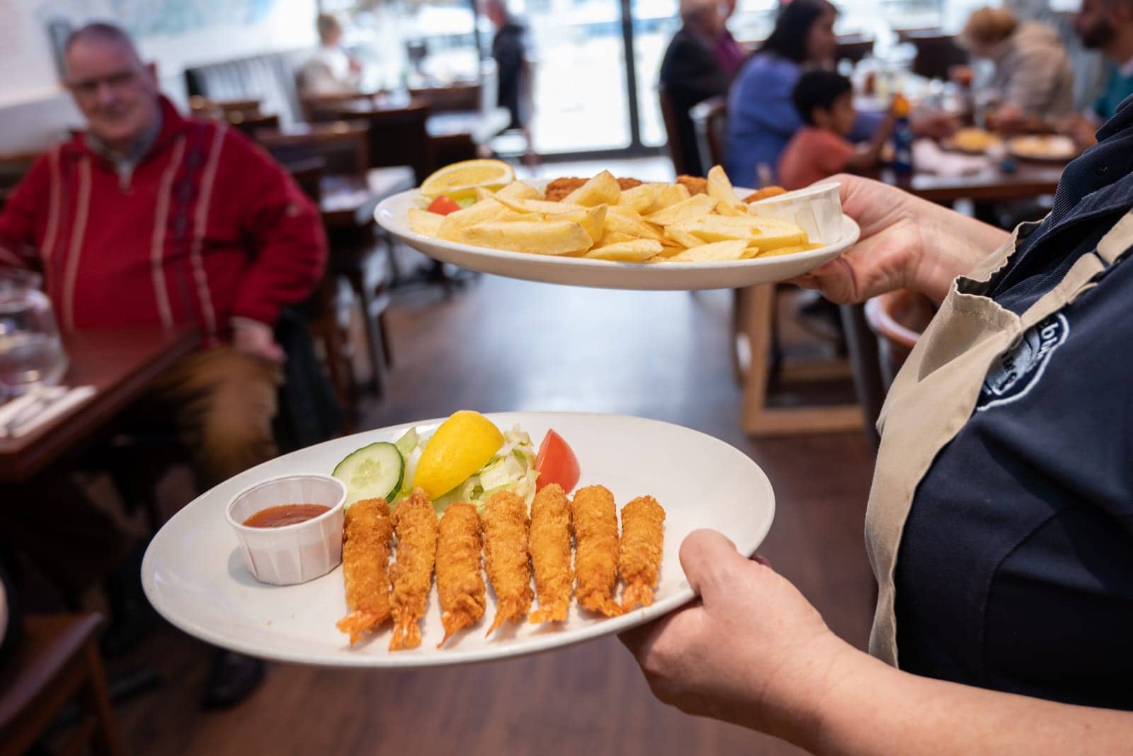 A member of the team carrying plates of cod goujons and chips to a table